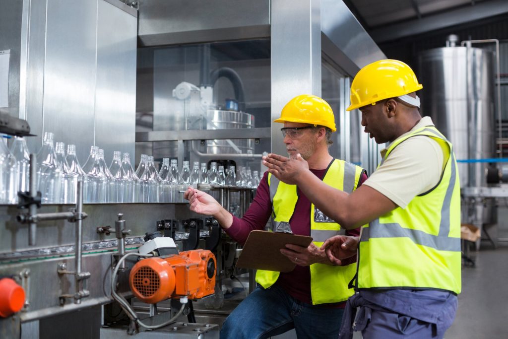 Two men wearing safety goggles and security vests manufacturing glass bottles