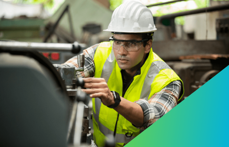 A technician in safety gear operates the controls of a piece of heavy industrial machinery on a factory floor.