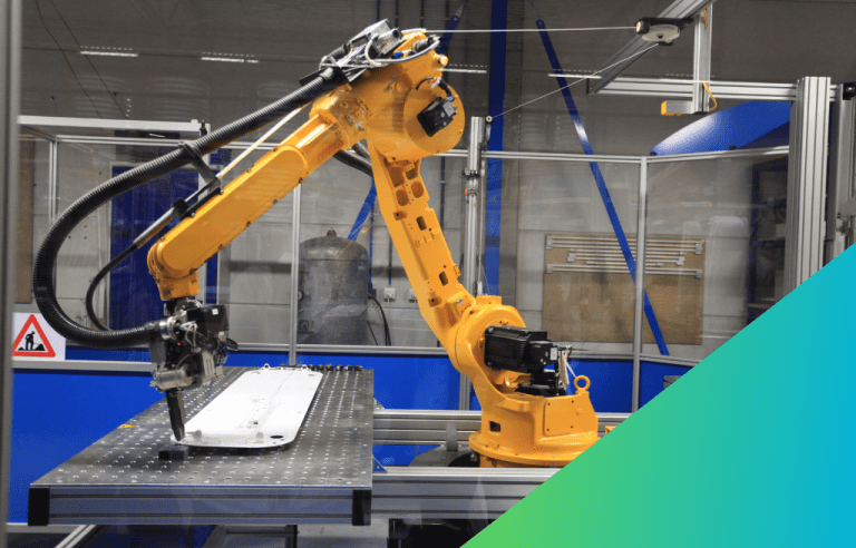 A yellow industrial robotic arm is performing a task on a component placed on a metal work table within a protected work cell.
