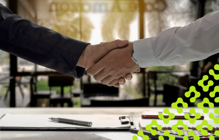 Close up of a handshake, and a pen laying on paperwork on a clipboard.