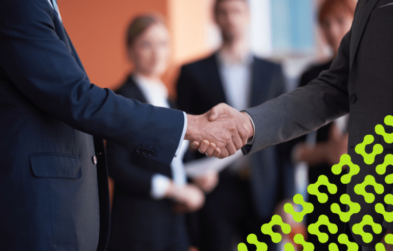 Close-up of two individuals in business suits shaking hands with three blurry people in the background.