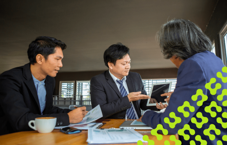 Three businessmen discussing on paperwork while looking at a tablet.