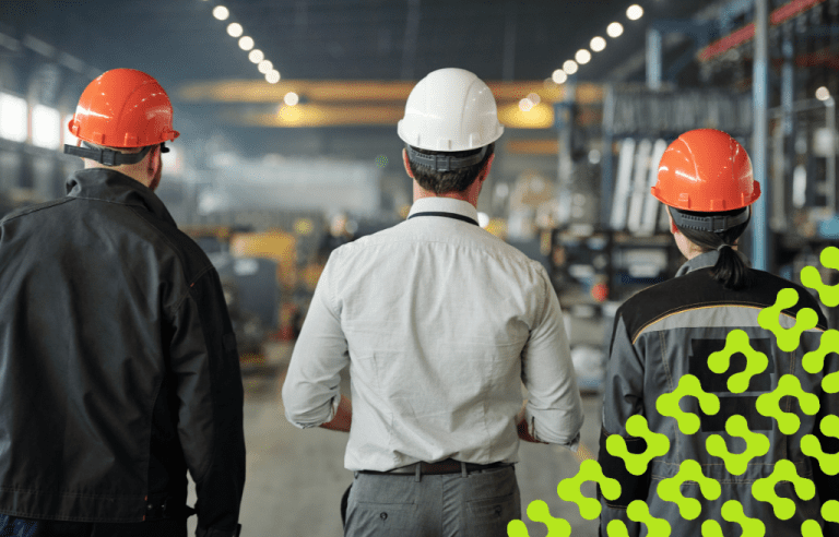 Three factory worker in hard hats and safety vest standing in a manufacturing area.