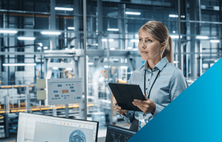A woman holding a tablet stands in a brightly lit industrial factory looking out at the machinery.