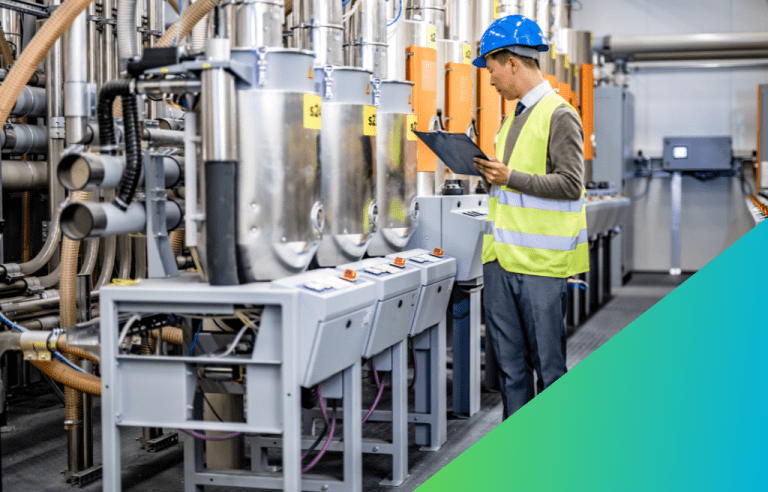 A worker in a hard hat and safety vest reviews a document on a clipboard while standing next to industrial processing equipment and its control panels in a manufacturing facility.
