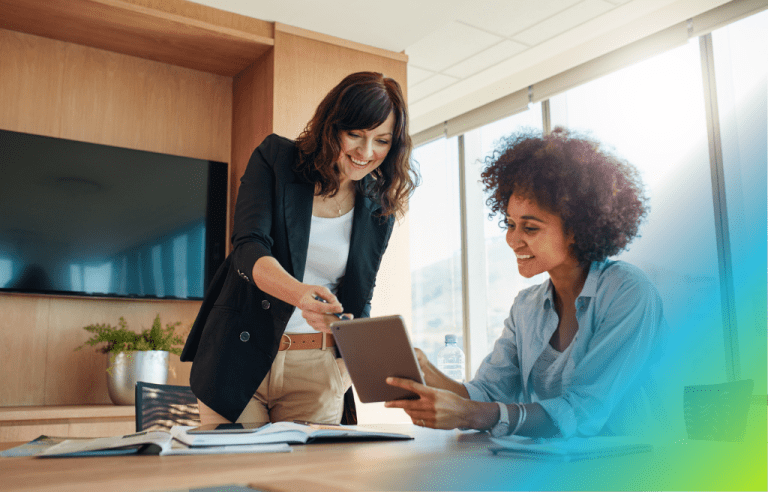 Two business women looking at a tablet together in a professional, light-filled environment office.