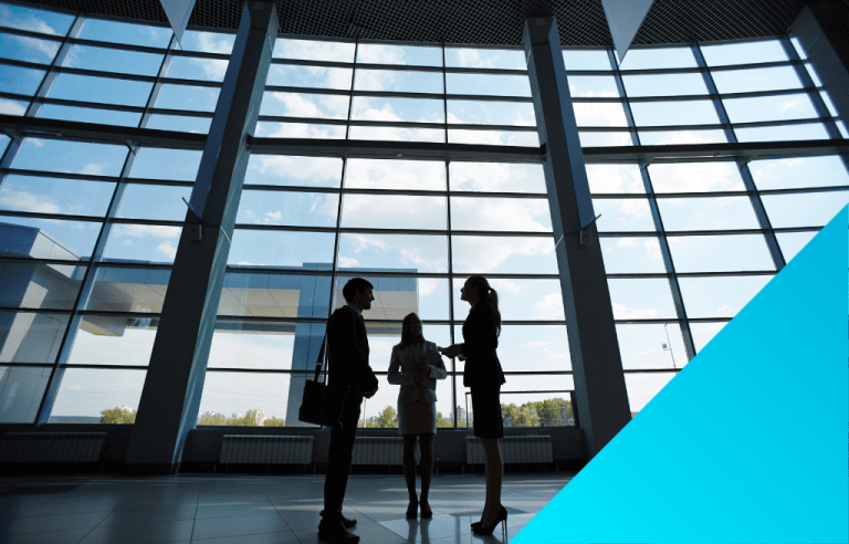 The silhouettes of three business people standing in front of a large window conversing.
