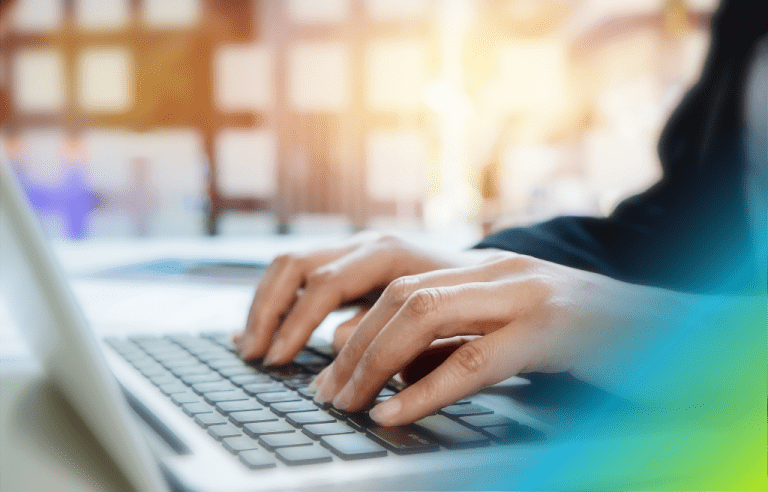 Close-up of a woman's hands typing on a laptop keyboard in a brightly lit environment.
