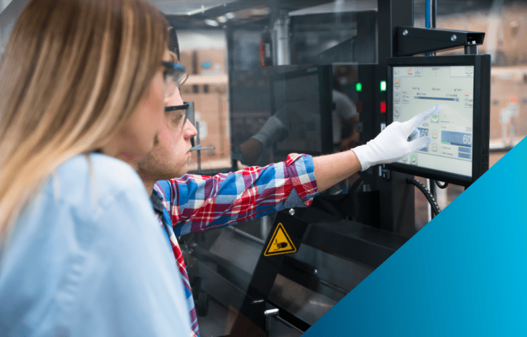Two technicians, one pointing with a gloved hand, review a control panel displaying real-time operational data for an automated manufacturing machine.
