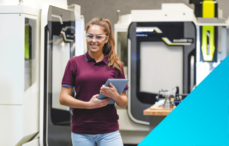 woman wearing protective eyewear while holding a tablet standing and smiling in front of modernized mechanical machines.