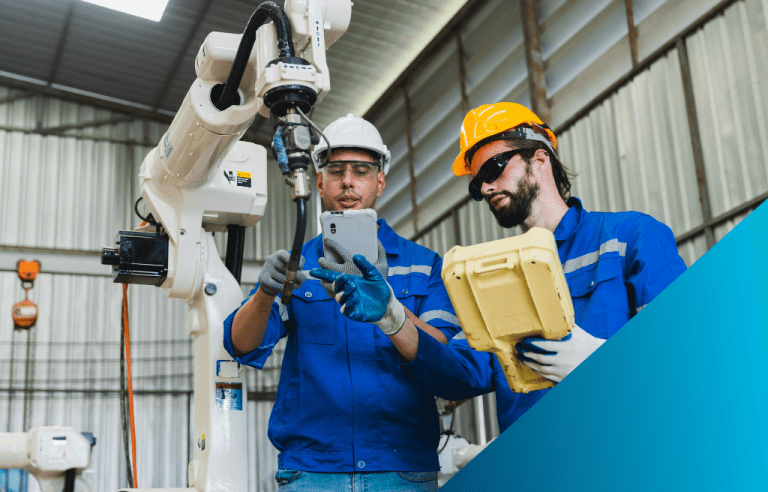 Two maintenance engineers are using a tablet and a teach pendant to program a collaborative robot on a factory floor.