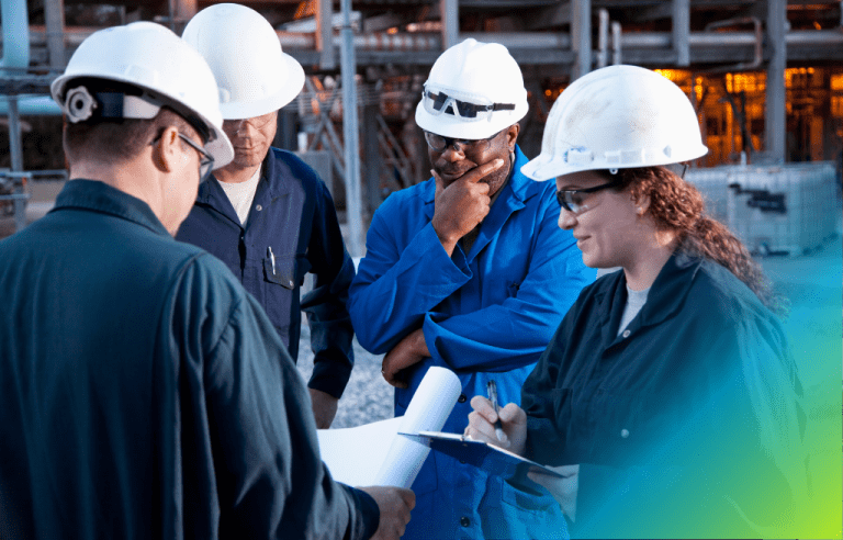 A group of construction managers in white hard hats reviewing plans on a construction site.