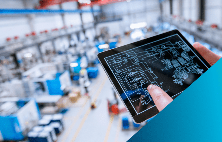 A close up of a person's finger pointing to a table that presents blueprints, while overseeing a blurry view of a factory floor.