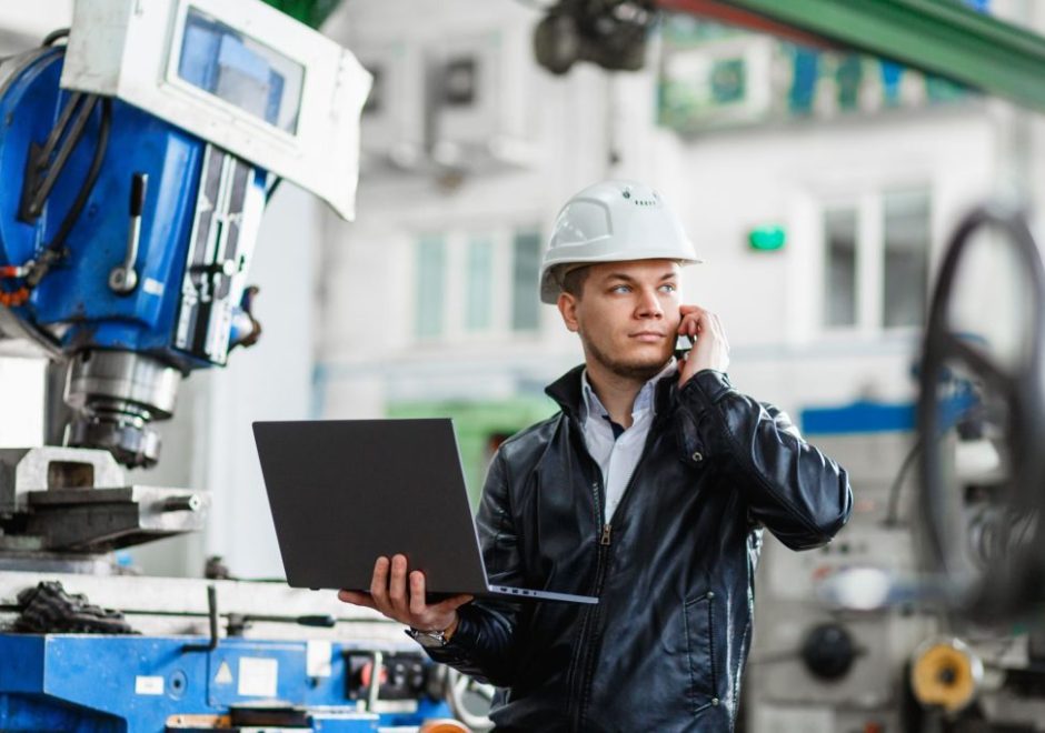 Man wearing a helmet while taking a phone call and using a laptop at a manufacturing plant